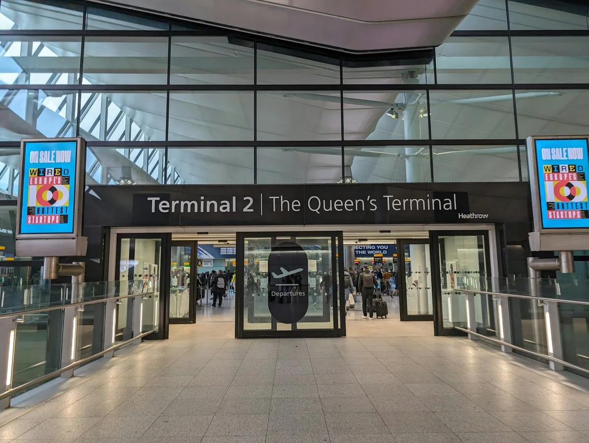 Entrance to Heathrow Terminal 2, The Queen's Terminal, with travellers inside the glass doors