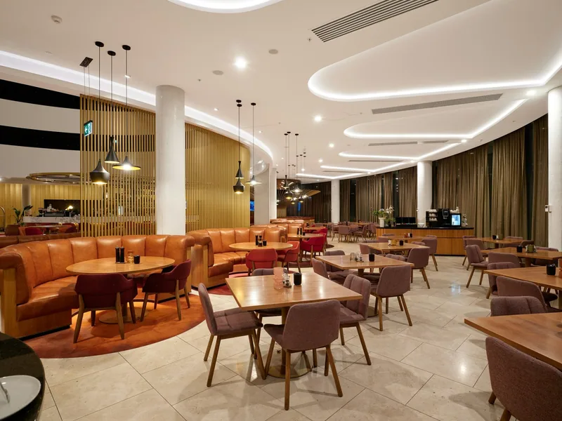 Inside an airport lounge with curved booth seating, dining tables and warm lighting