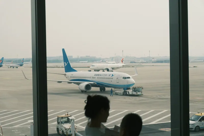 A child and an adult at a terminal window watching an aircraft being loaded on the apron