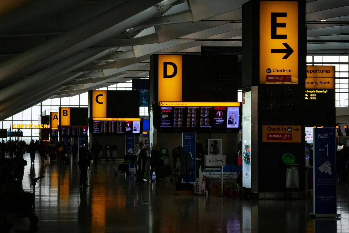 Yellow check-in zone signs lettered C, D and E in a Heathrow terminal departures hall