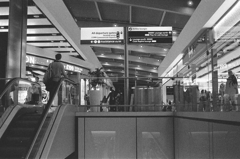 Black and white view of escalators and travellers inside Heathrow Terminal 5