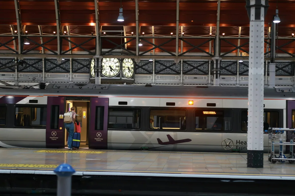 Passenger boarding a Heathrow Express train beneath the clock at Paddington station