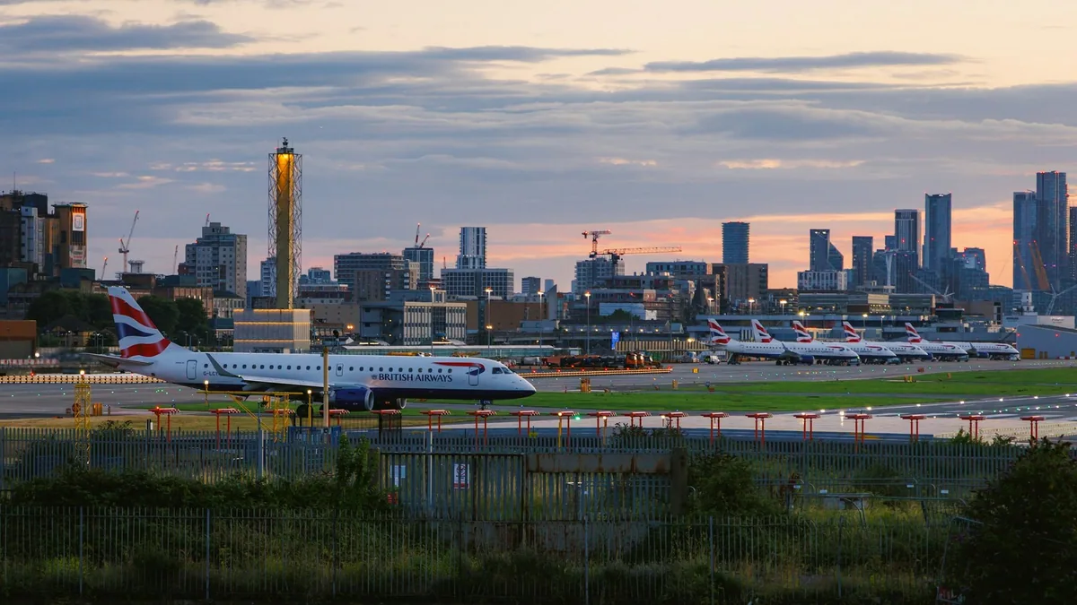British Airways jet lining up on the London City Airport runway with the Canary Wharf skyline behind