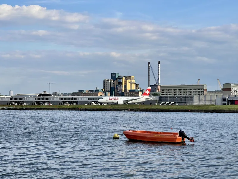 The London City Airport terminal and its apron with a single airliner beside it, seen across the water of the Royal Albert Dock