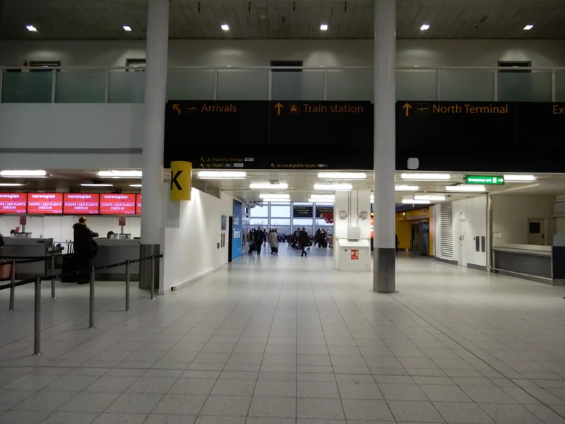 Gatwick South Terminal concourse with overhead signs pointing to arrivals, the train station and North Terminal