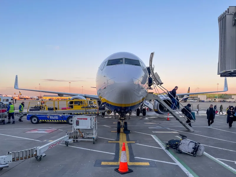 Passengers boarding a Boeing 737 by the rear and front stairs on the Stansted apron at sunset