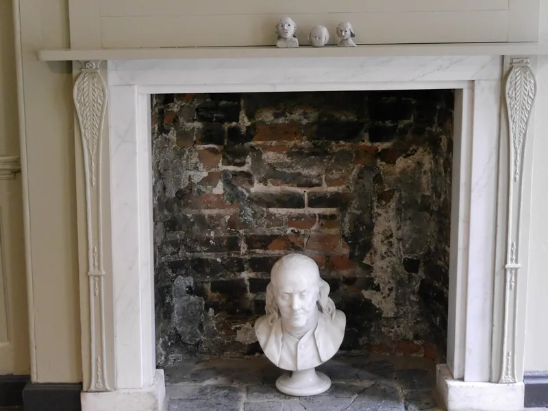 A marble bust of Benjamin Franklin standing in the bare brick hearth of a fireplace in the house