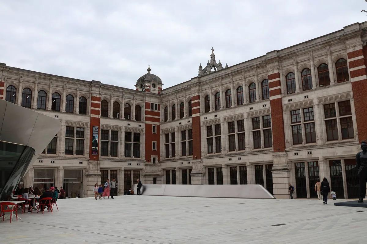 The Sackler Courtyard at the Victoria and Albert Museum, with cafe tables on the pale tiled yard below the red-brick screen
