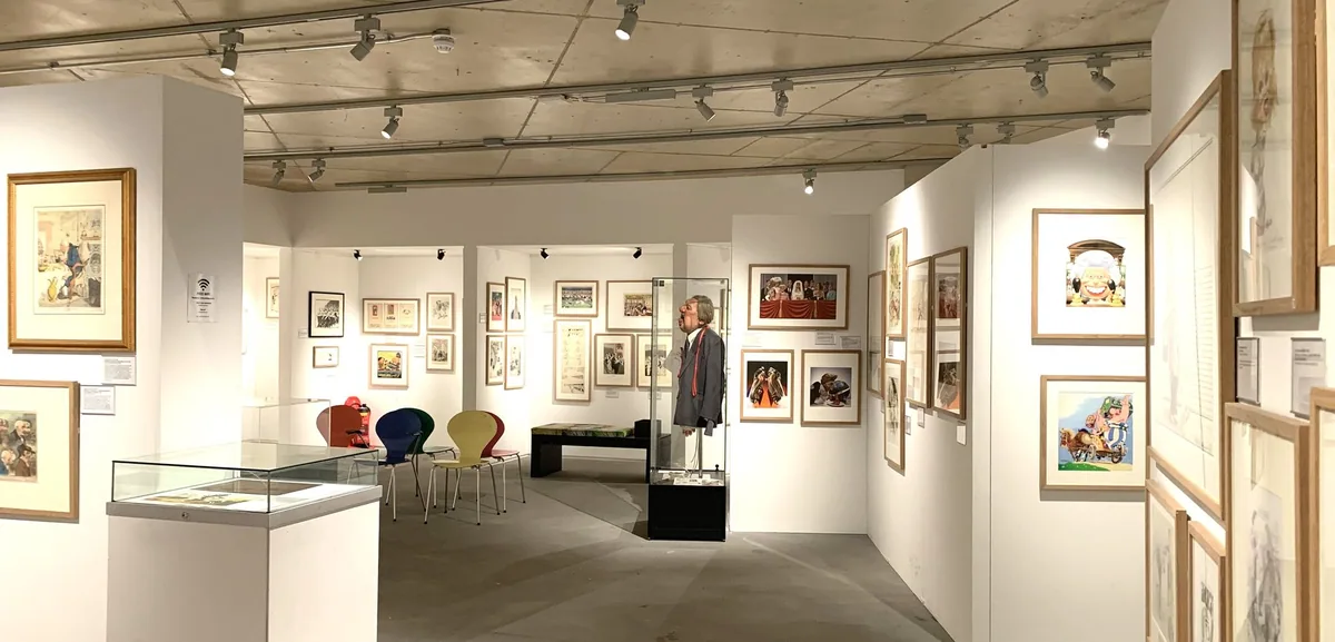 White gallery walls hung with framed cartoons and a puppet in a display case at the Cartoon Museum