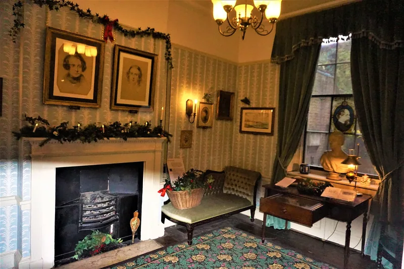 The morning room at the Charles Dickens Museum with a writing desk, green sofa and portraits above the fireplace