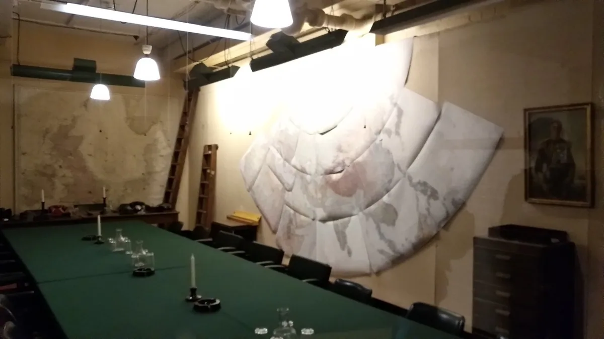 Long green-topped conference table beneath wall maps in an underground meeting room at the Churchill War Rooms