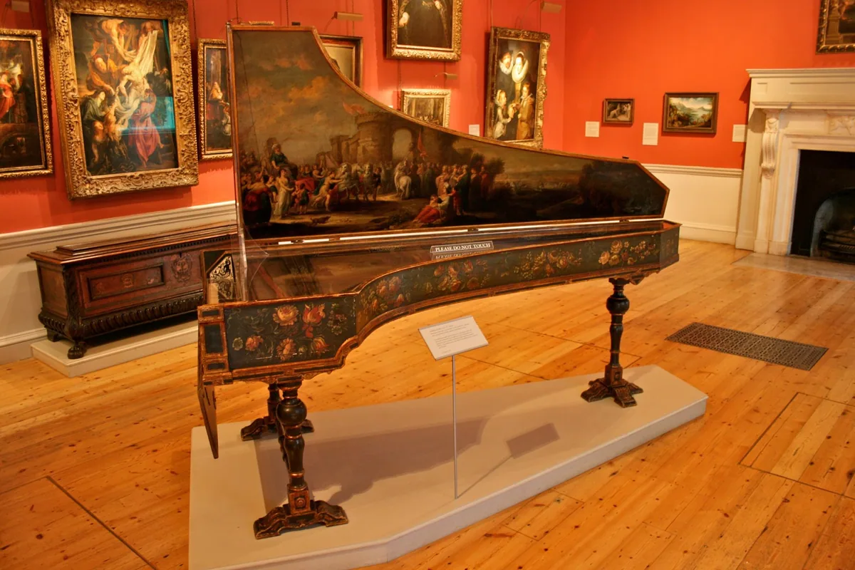 A painted 17th-century harpsichord in a red-walled gallery hung with gilt-framed paintings at the Courtauld