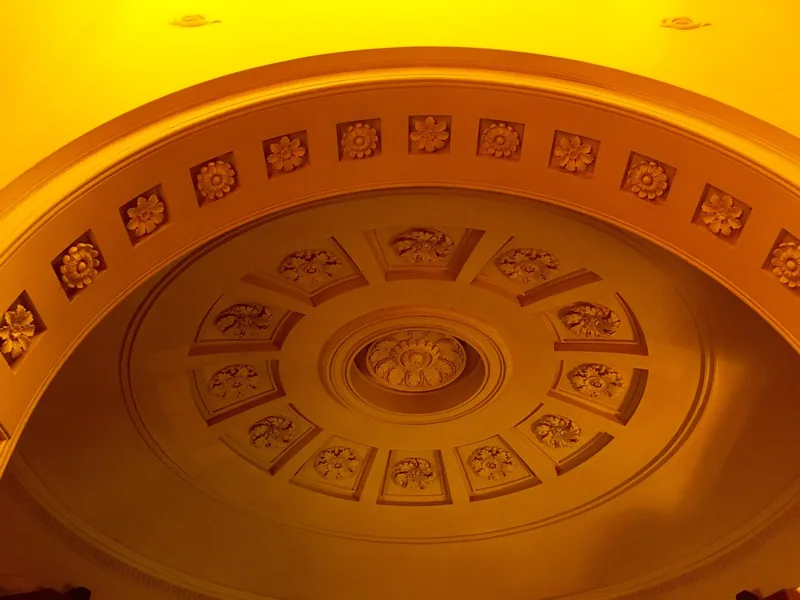 A coffered dome of plaster rosettes lit amber from above inside Dulwich Picture Gallery