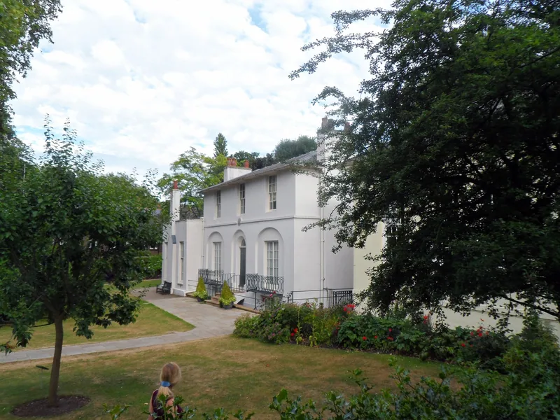 Keats House viewed across its lawned garden with trees and a winding path in Hampstead