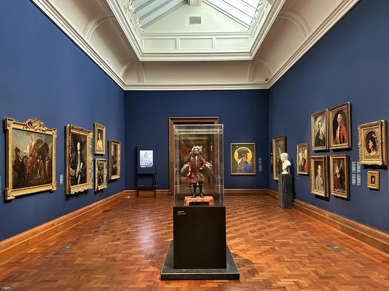 Skylit gallery room with blue walls, parquet floor and gilt-framed historic portraits in the National Portrait Gallery