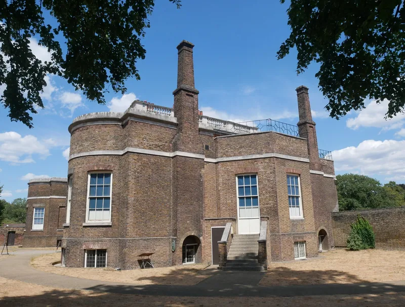 The brown-brick south-west side of Ranger's House, with its curved bay and two tall chimney stacks, framed by park trees