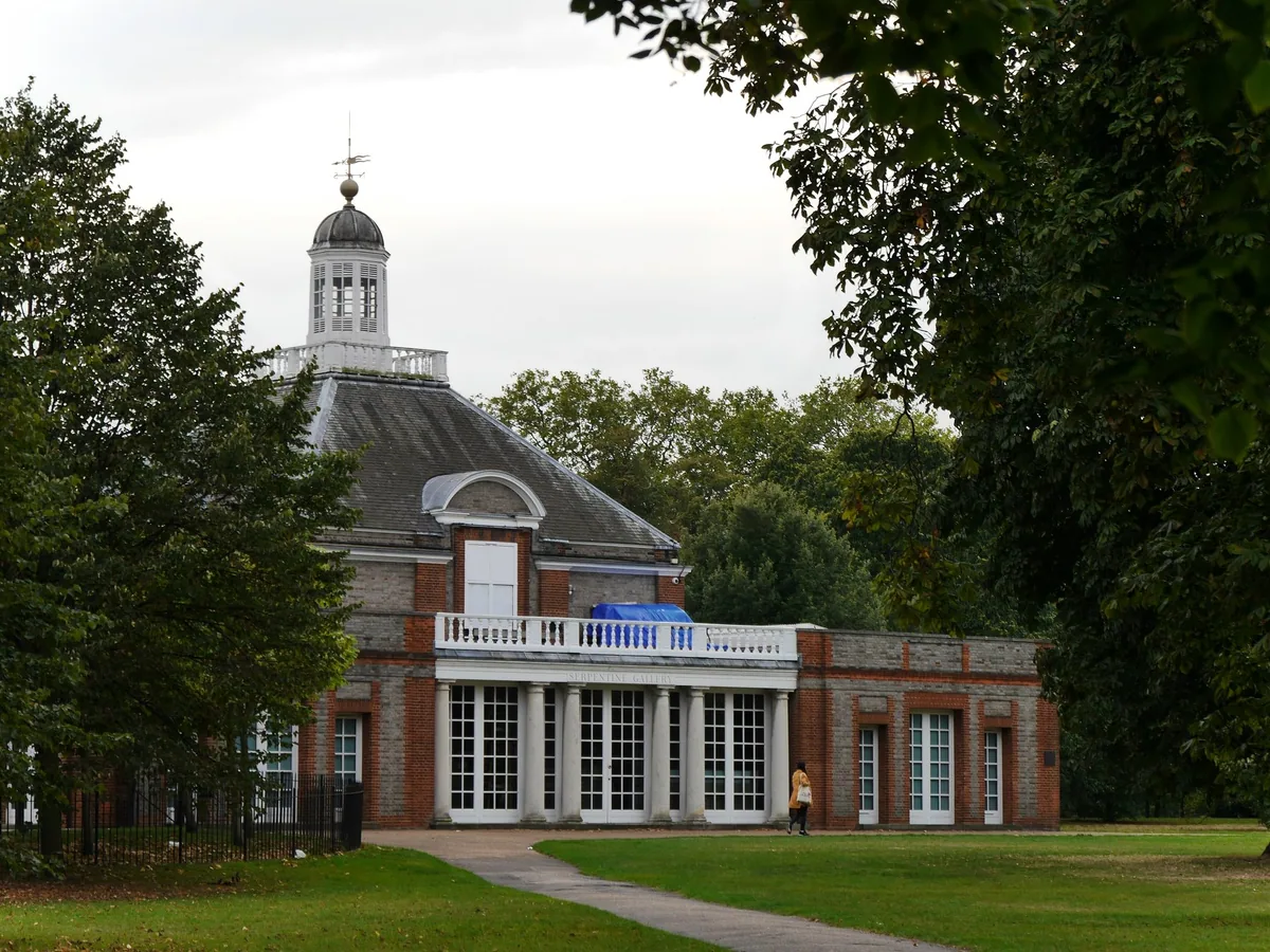 The brick and stone Serpentine Gallery pavilion with its cupola, seen across the lawns of Kensington Gardens
