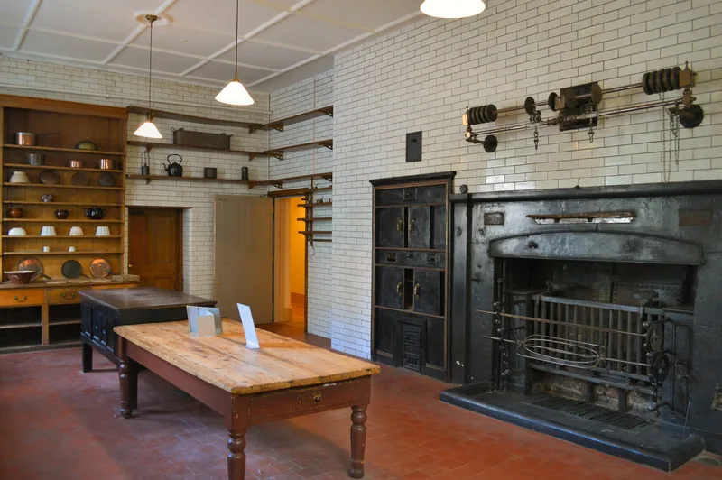 Restored Victorian kitchen with a cast-iron range, tiled walls, scrubbed pine table and shelves of copper pans