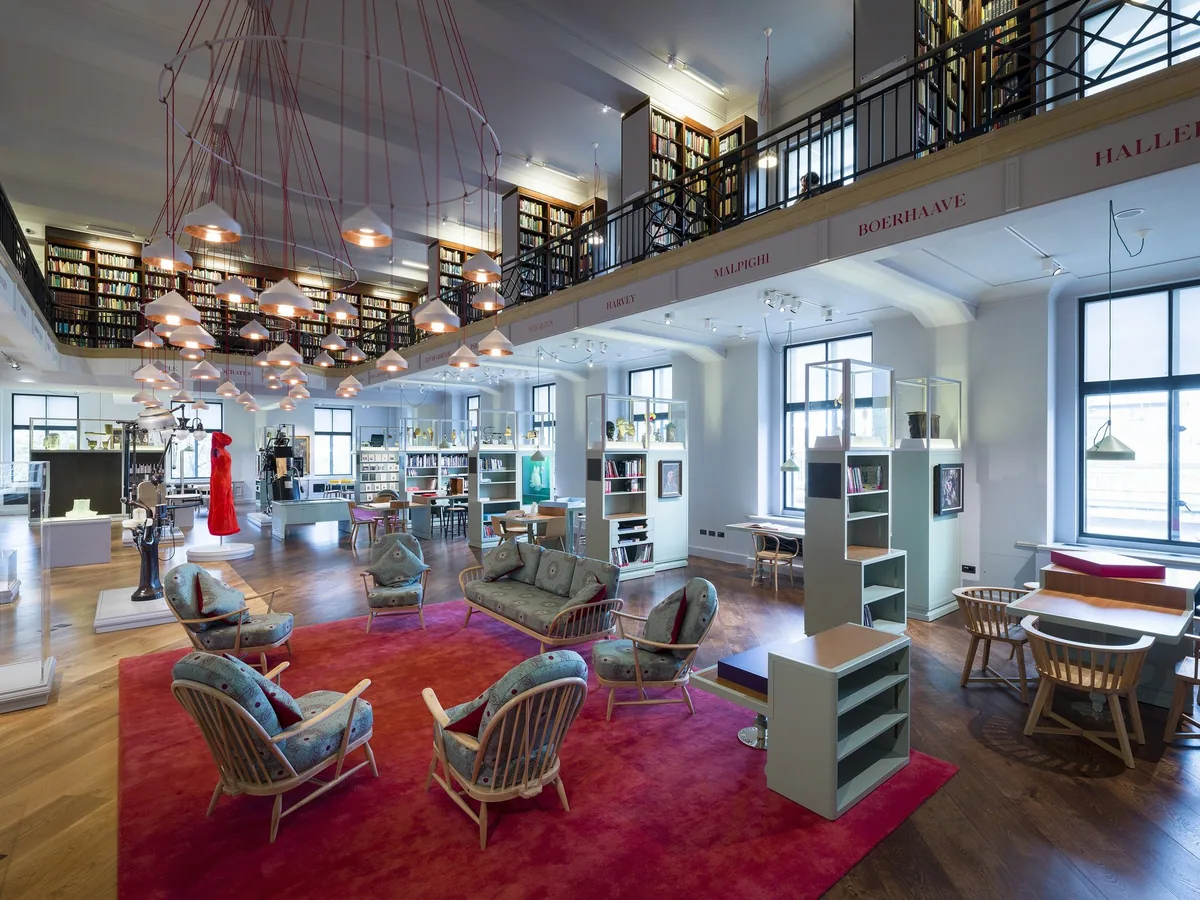 The Reading Room at Wellcome Collection with armchairs on a red carpet, bookshelves and hanging lamps