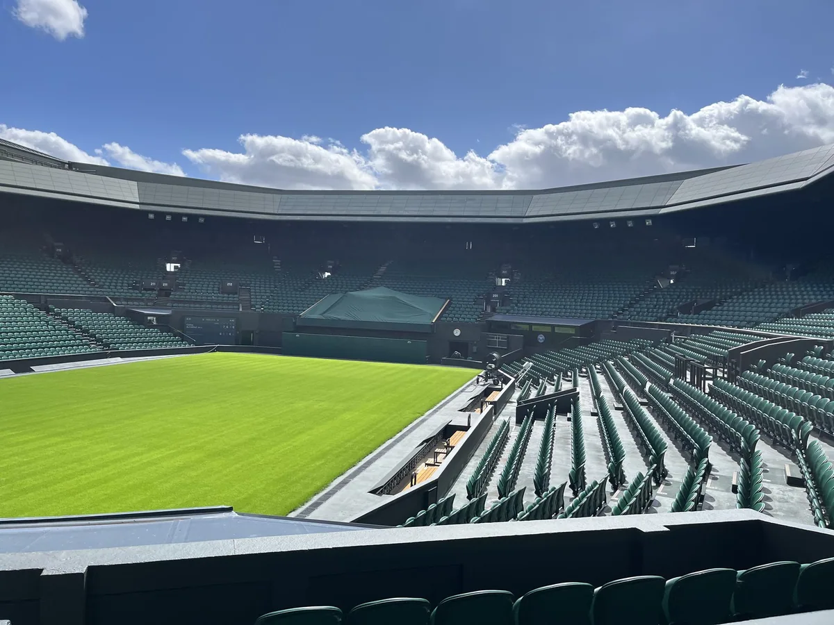 Empty Centre Court at Wimbledon, its grass freshly mown and the green seats deserted