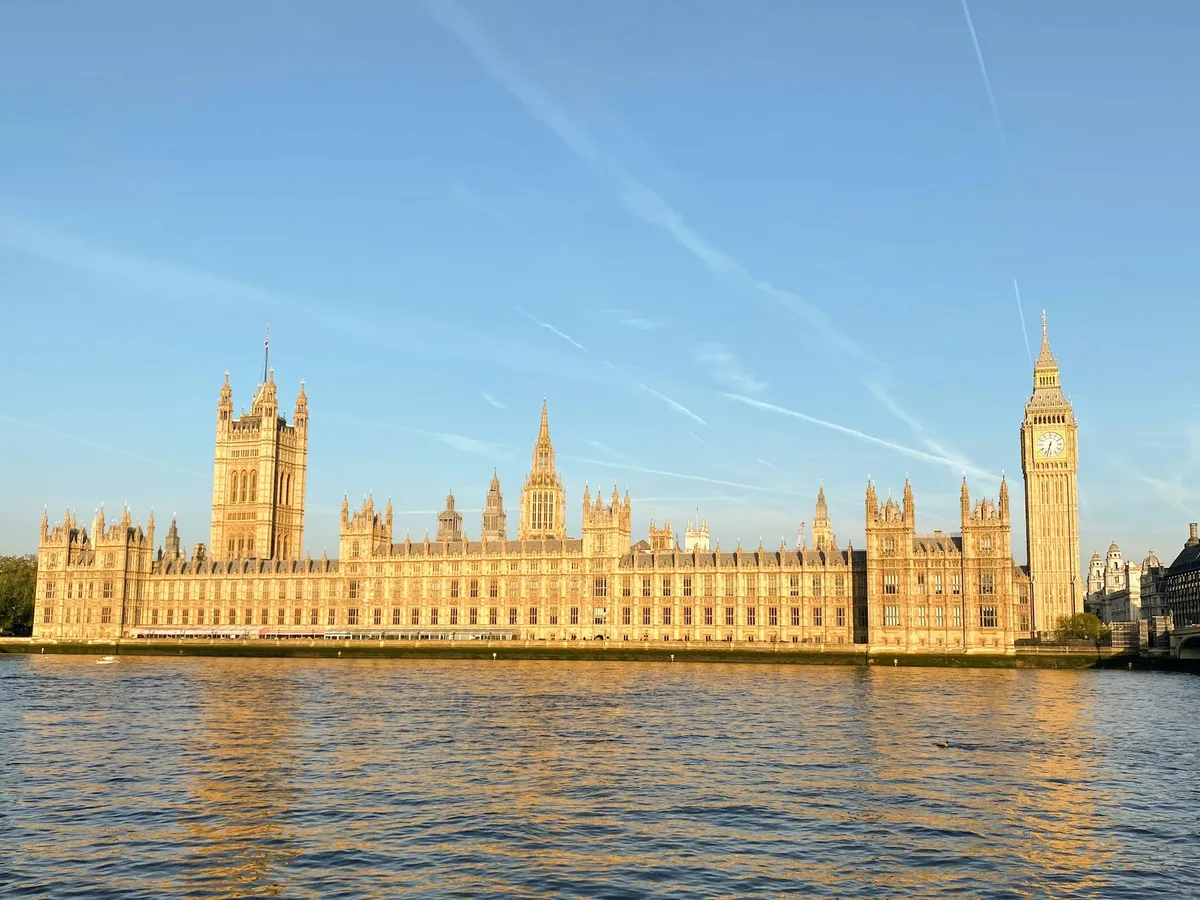 The Palace of Westminster and Elizabeth Tower glowing in morning sunlight across the Thames