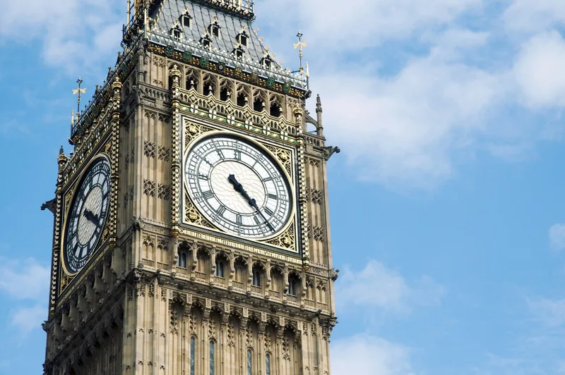 Close-up of the gilded clock faces near the top of the Elizabeth Tower against a blue sky