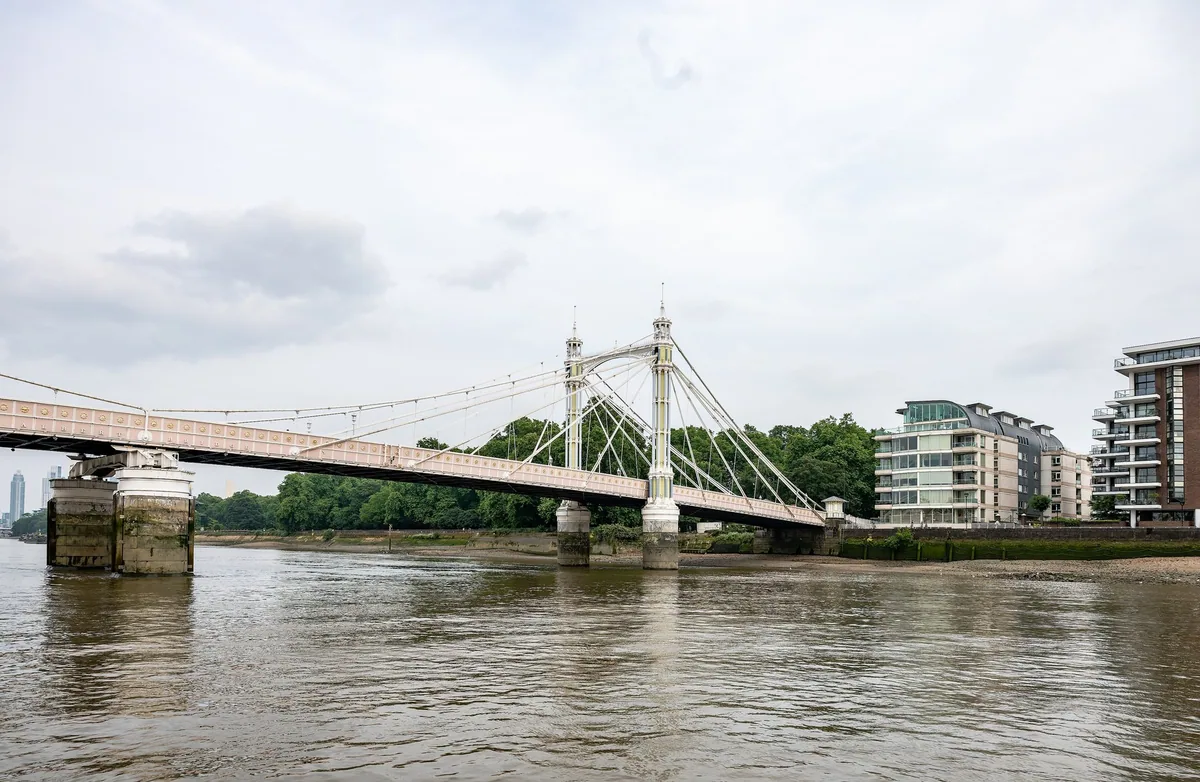 The pale pink span of Albert Bridge across the Thames at low tide, its two ornate towers and cable stays seen side-on