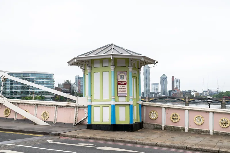 The green and blue octagonal tollbooth on Albert Bridge, carrying the notice telling troops to break step, with the pink parapet beside it