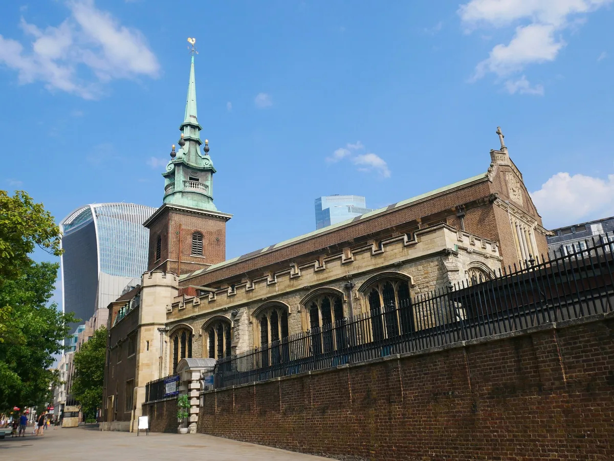 All Hallows-by-the-Tower seen from the south-east, its brick tower and green copper spire against City skyscrapers