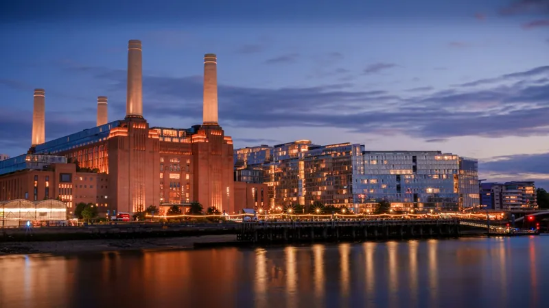 Battersea Power Station floodlit at dusk, with the new riverside apartment blocks reflected in the Thames