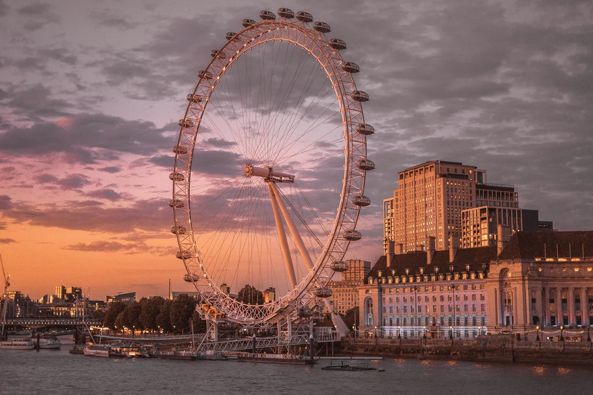 The London Eye beside County Hall on the Thames, lit by a pink and orange sunset sky
