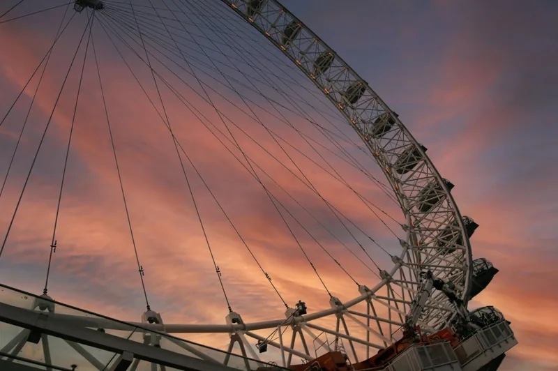 Looking up at the London Eye's rim, spokes and capsules against a streaked orange sunset sky