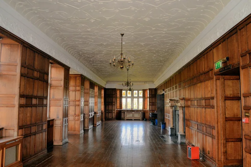 The oak-panelled Long Gallery inside Charlton House, with a moulded plaster ceiling, a chandelier and a window at the far end