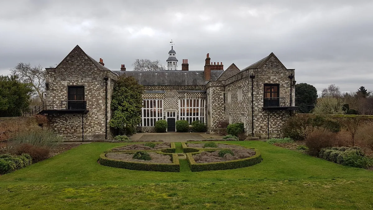 The chequered flint and stone Tudor front of Hall Place in Bexley, with a clipped box knot garden on the lawn before it
