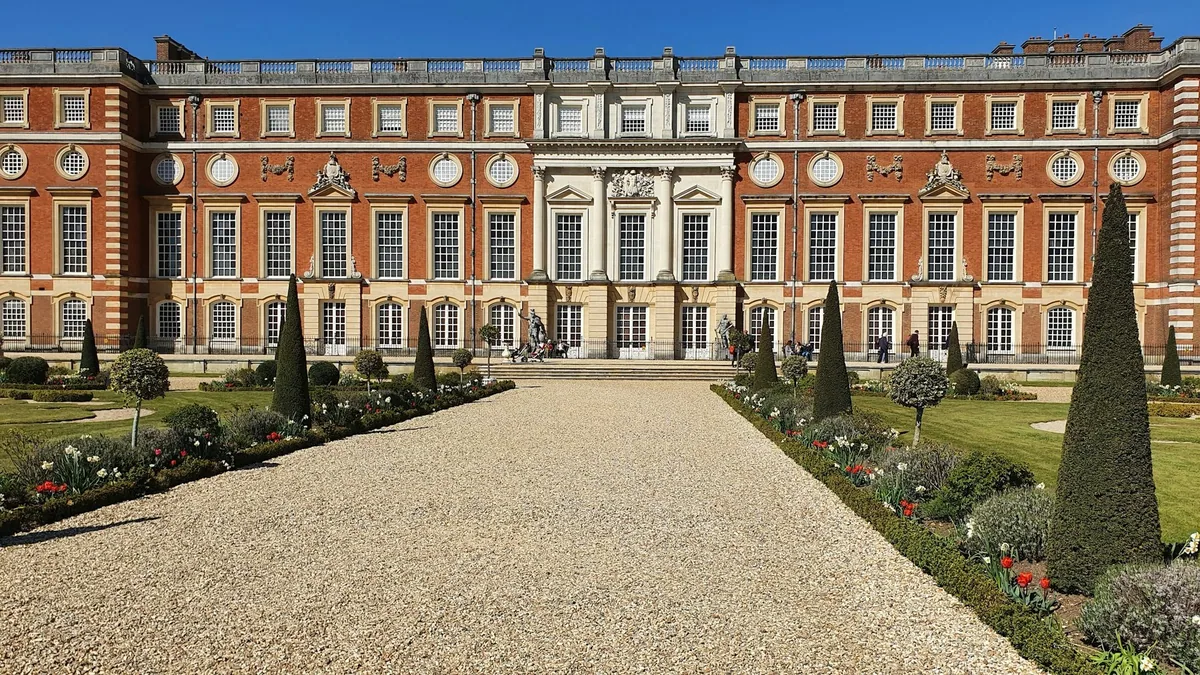 A gravel path between clipped yews leading to the red-brick Baroque front of Hampton Court Palace