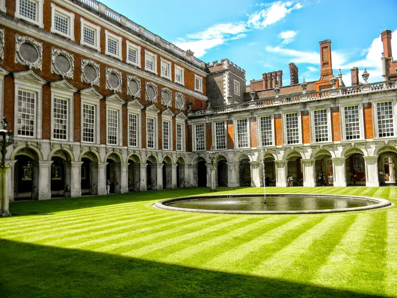 Fountain Court at Hampton Court Palace, with a round pool and striped lawn inside arcaded brick wings