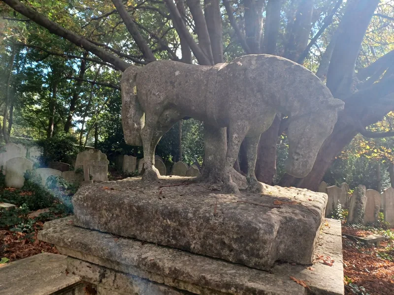 A weathered stone lion lying on a Victorian tomb in the wooded West Cemetery at Highgate