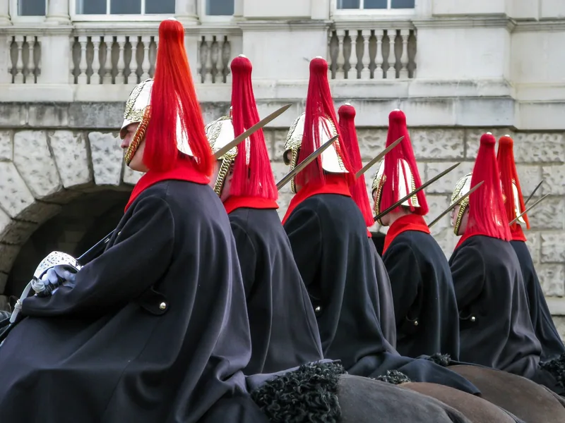 A line of mounted Household Cavalry troopers in dark cloaks and red-plumed helmets at Horse Guards