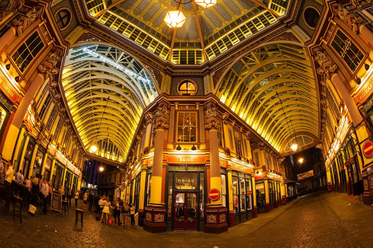 The painted ironwork and glass roof at the central crossing of Leadenhall Market, with office workers on the cobbles