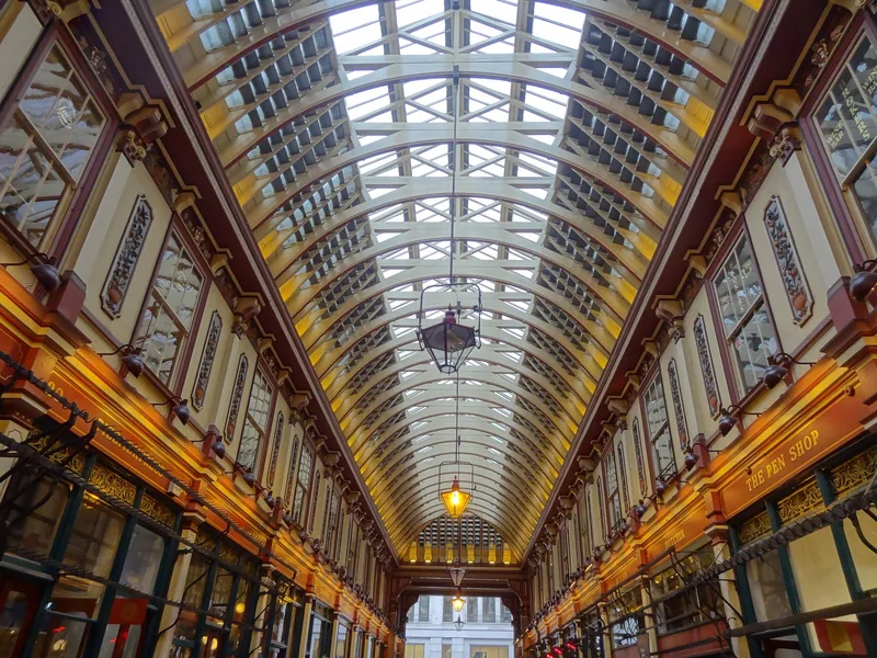 Looking down an arcade of Leadenhall Market, hanging lanterns beneath the arched glass and iron roof