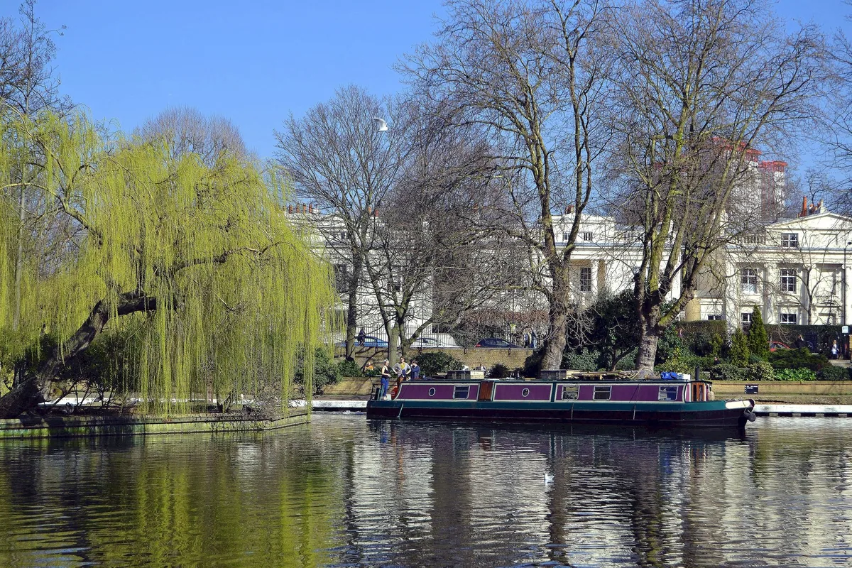 A narrowboat on the water at Little Venice, with a weeping willow on the left and white stucco houses behind