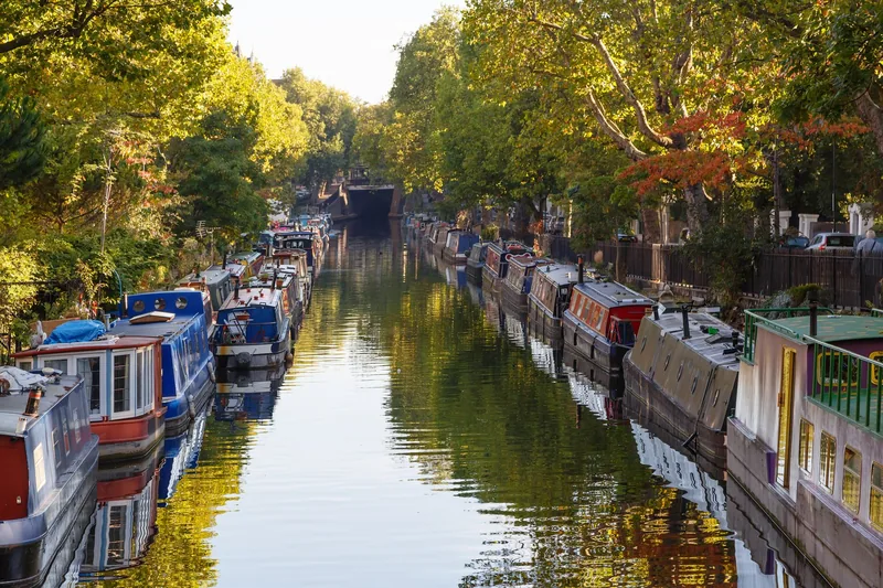 Narrowboats moored along both banks of the canal at Little Venice under autumn trees