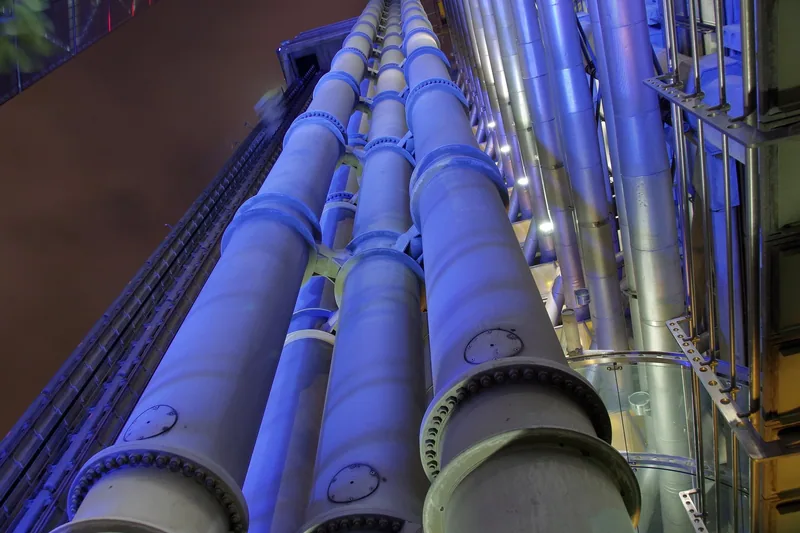 Banks of steel service pipes on the north face of the Lloyd's Building, lit blue after dark