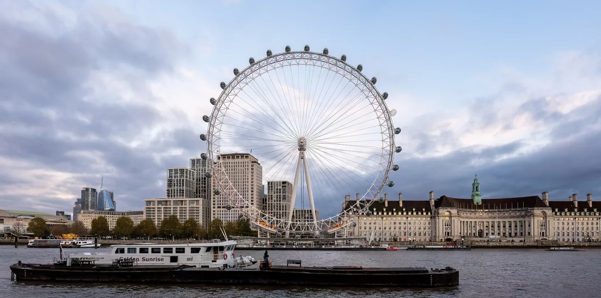 The London Eye standing beside the Thames with its capsules on the rim, County Hall along the bank to the right