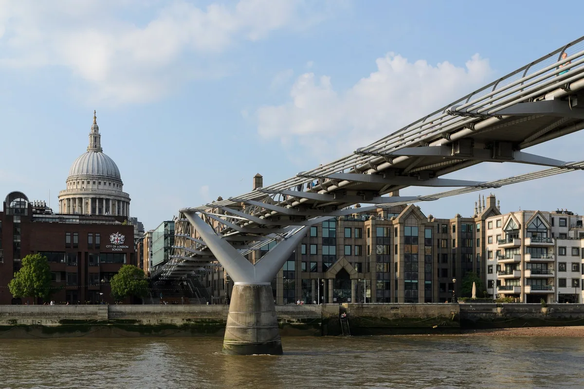 The Millennium Bridge from the Thames, its steel arms and Y-shaped river pier in profile, with the dome of St Paul's beyond