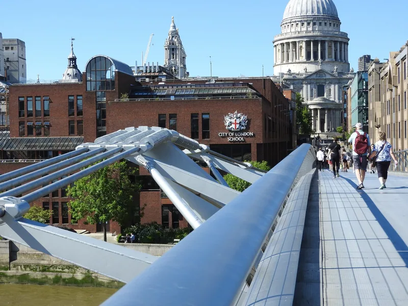 Walking north across the Millennium Bridge: the aluminium deck and steel balustrade, people ahead, and St Paul's dome at the end