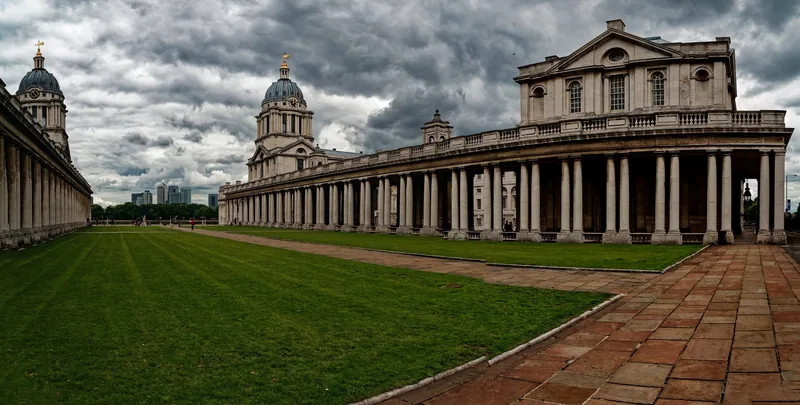 The long colonnade and dome of the Old Royal Naval College beside the lawn, with Canary Wharf in the distance