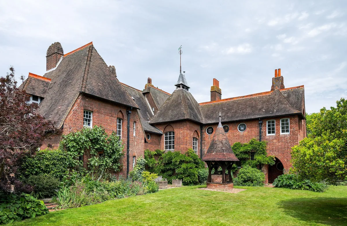 Red House at Bexleyheath from the garden: steep red-tiled roofs over red brick, with Webb's conical timber well head on the lawn