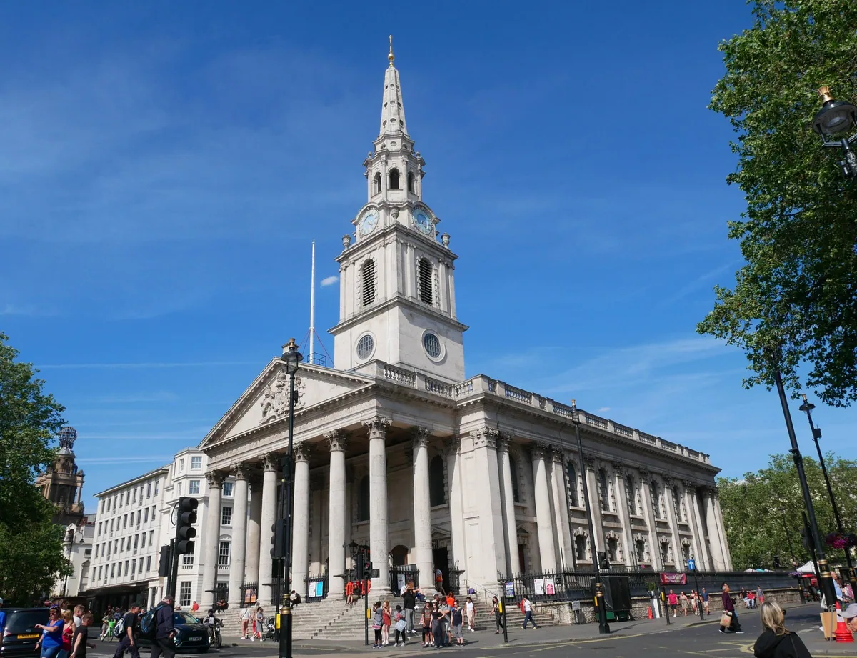 The columned portico and tall white steeple of St Martin-in-the-Fields beside Trafalgar Square under a blue sky