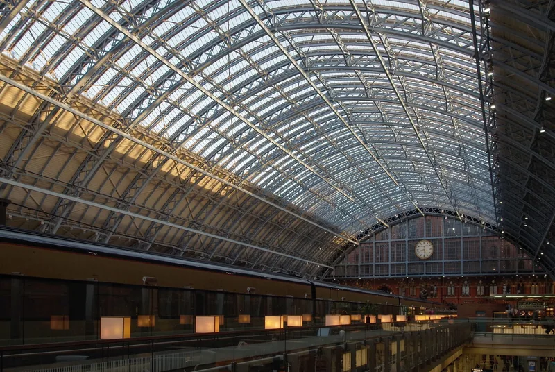The curved iron and glass roof of the Barlow train shed inside St Pancras station, with the station clock